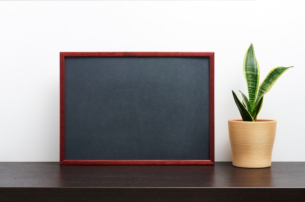 Cadre en bois brun ou maquette de tableau en orientation paysage avec un cactus dans un pot sur la table de l'espace de travail sombre et fond blanc