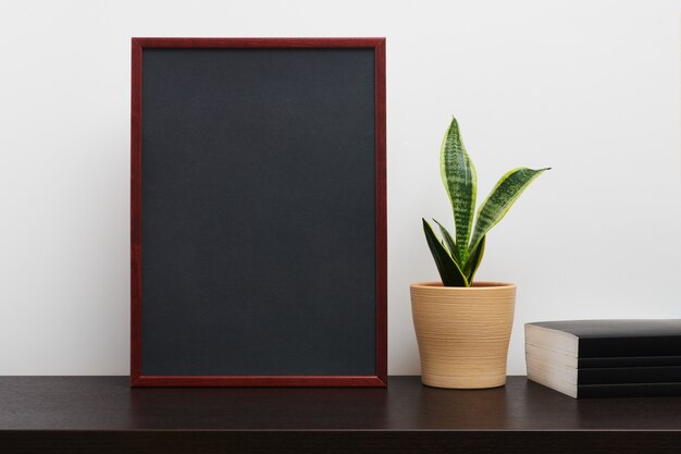 Cadre en bois brun ou maquette de tableau en orientation portrait avec un cactus dans un pot et livre sur la table de l'espace de travail sombre et fond blanc