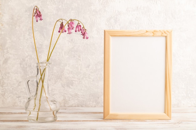 Cadre en bois avec dicentra rose, coeur brisé en verre sur fond de béton gris. vue de côté