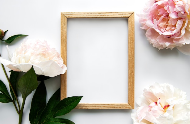 Cadre en bois entouré de belles pivoines roses sur fond blanc, vue de dessus, espace copie, mise à plat. Carte de voeux maquette, invitations à des vacances ou à un mariage. Concept de fleur d'été lumineux.