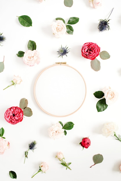 Cadre de broderie avec motif de boutons de fleurs roses rouges et beiges sur fond blanc. Mise à plat, vue de dessus