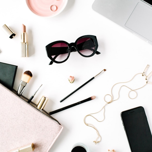 Cadre De Bureau De Table De Bureau Plat Lapointe, Vue De Dessus. Espace De Travail De Bureau Féminin Avec Ordinateur Portable, Pochette, Cosmétiques, Téléphone, Lunettes De Soleil, Boutons De Rose Rouge à Lèvres Sur Fond Blanc.