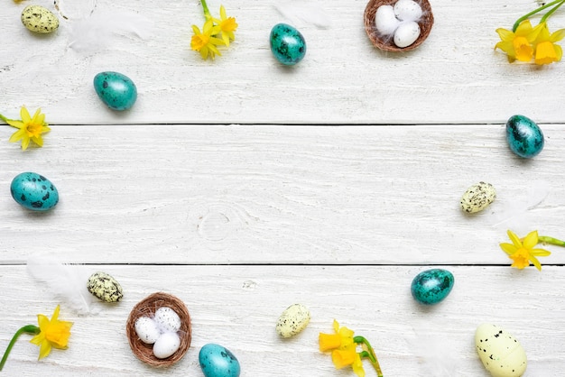 Cadre composé d'oeufs de Pâques et de fleurs de printemps sur une table en bois blanc. composition de pâques