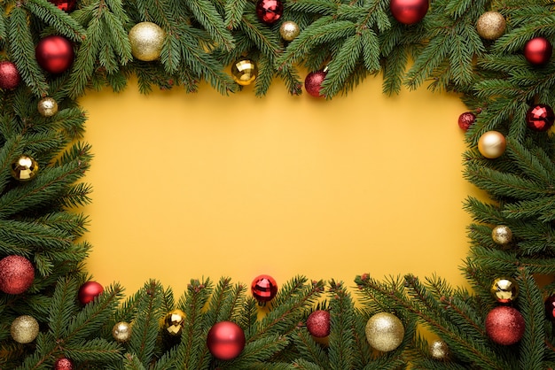 Cadre décoratif de boules de Noël et de branches de sapin. Fond jaune pour la conception de Noël et du nouvel an. Copiez l'espace pour les promotions, la publicité et le texte de félicitations