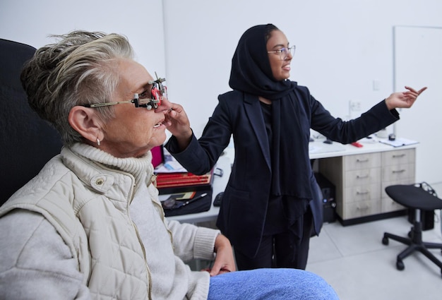 Photo cadre d'examen de la vue et femme lisant avec un optométriste en clinique pour un test de vision et une évaluation optique soins de santé en optométrie et opticien musulman avec patient dans des verres de lunettes et un outil médical