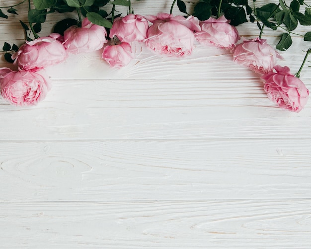 Cadre fait de fleurs roses roses sur un fond en bois blanc.