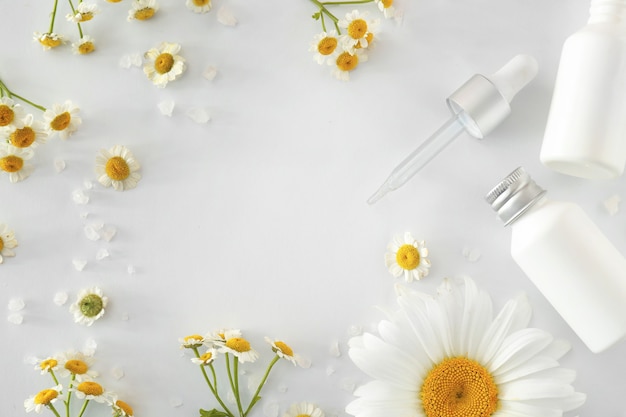 Cadre fait de produits cosmétiques avec des fleurs de camomille sur fond blanc