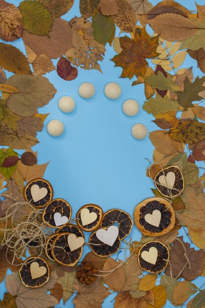 Photo cadre de feuilles d'automne avec des tranches d'agrumes secs d'oranges et de mandarines et des coeurs en bois sur fond de papier bleu