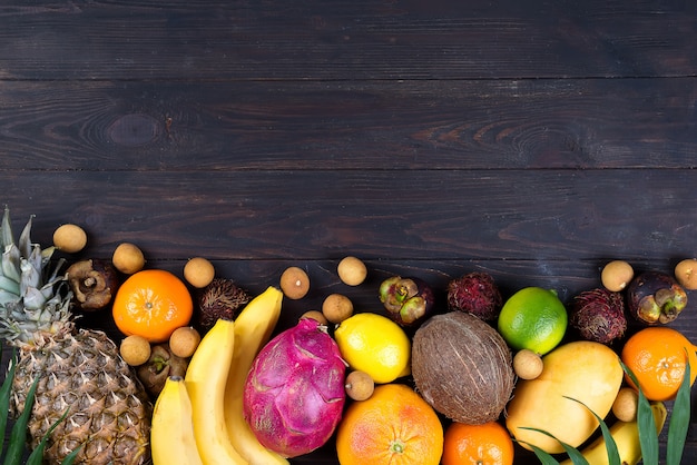 Cadre de fruits tropicaux arc-en-ciel en bonne santé avec des feuilles de palmier sur une table en bois bleue