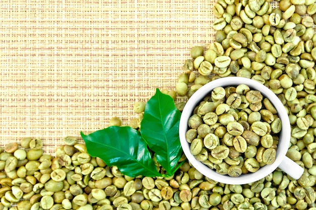 Un cadre de grains de café verts avec des feuilles et une tasse sur un tissu tissé grossier jaune