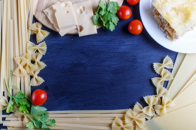 Cadre avec des ingrédients de pâtes italiennes sur un fond en bois noir.