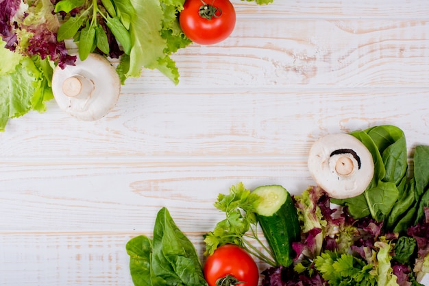 cadre de légumes frais, laitue, tomate, concombre, champignons, persil, épinards sur un bois blanc