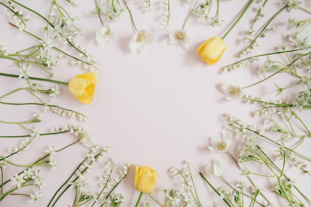 Cadre de muguet, tulipes jaunes, feuilles vertes sur rose