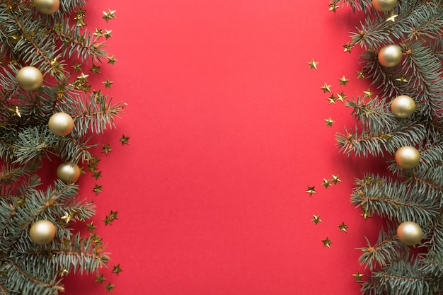 Cadre de Noël avec des branches de sapin, des boules d'or sur fond rouge.