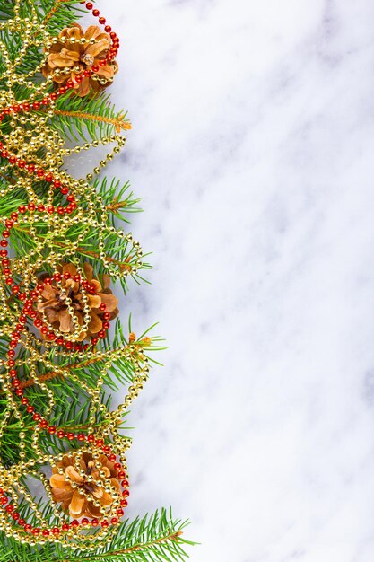 Cadre de Noël avec des branches de sapin et des perles rouges sur fond blanc. Cadre de Noël de branches d'épinette et de pommes de pin sur fond de marbre. Collier doré. Espace de copie. Mise à plat