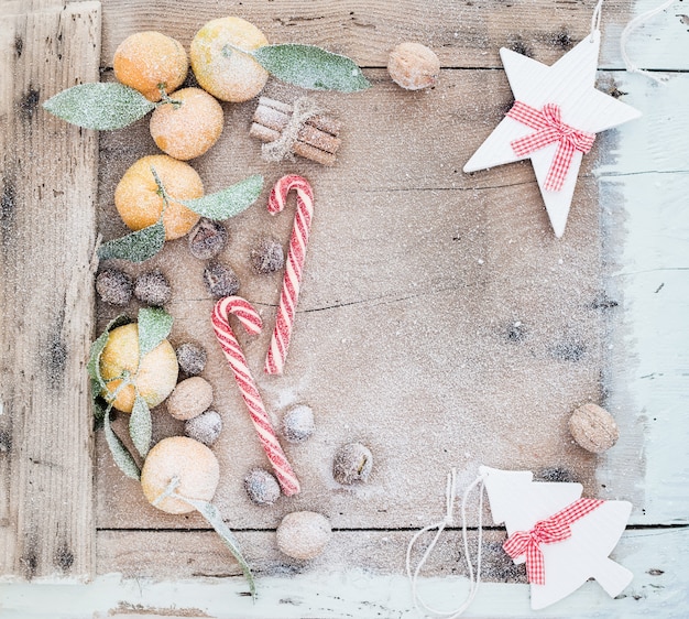 Cadre de Noël ou du nouvel an. Mandarines fraîches, bâtons de cannelle, noix, châtaignes grillées et cannes de bonbon recouvertes de neige sur une table en bois rustique