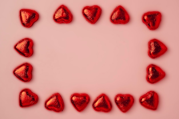 Un cadre de nombreux bonbons brillants en forme de coeur enveloppés dans du papier d'aluminium sur fond rose