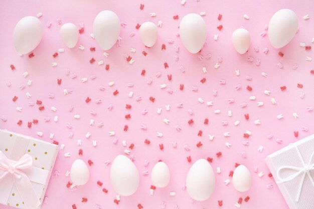 Photo cadre d'œufs de pâques avec des oreilles de lapin, du sucre et une boîte cadeau sur fond rose