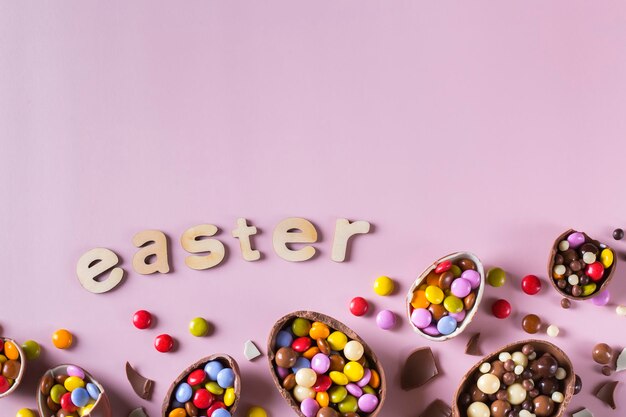 Cadre de Pâques avec des oeufs en chocolat et des bonbons sur fond rose. Joyeux texte de Pâques. Vue de dessus, mise à plat