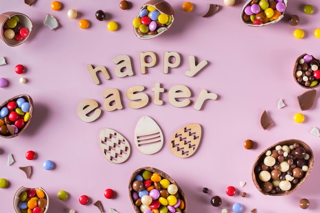 Cadre de Pâques avec des oeufs en chocolat et des bonbons sur fond rose Texte de Joyeuses Pâques Vue de dessus mise à plat