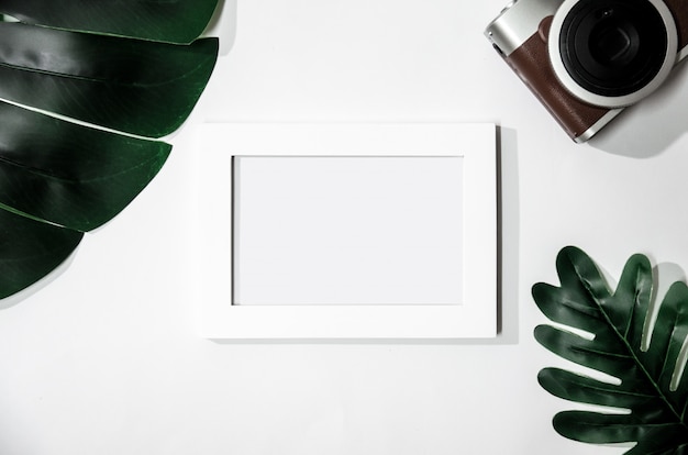 Cadre photo blanc avec feuilles vertes et caméra sur blanc isolé