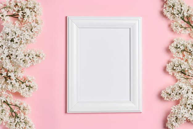 Cadre photo blanc vide et fleurs lilas blanches sur un mur rose.