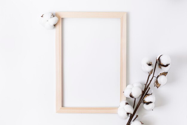 Cadre photo en bois avec une fleur de coton et un tissu blanc sur fond blanc