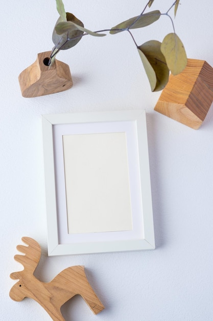 Cadre photo avec branche d'eucalyptus dans un vase en bois et jouet en bois sur fond blanc