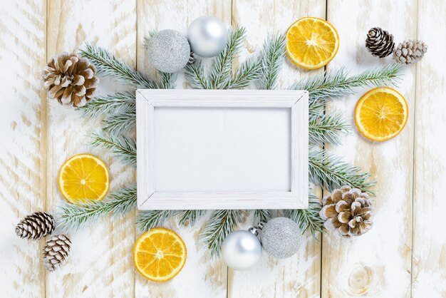 Cadre photo entre la décoration de Noël, avec des boules blanches et des pommes de pin sur une table en bois blanche. Vue de dessus, cadre pour copier l'espace