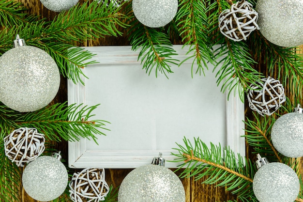 Cadre photo entre la décoration de Noël, avec des boules blanches sur une table en bois marron. Vue de dessus, cadre pour copier l'espace.