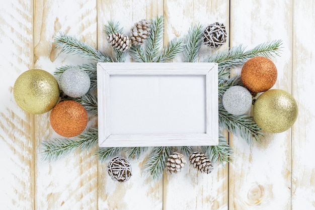 Cadre photo entre la décoration de Noël, avec des boules multicolores et des pommes de pin sur une table en bois blanche. Vue de dessus, cadre pour copier l'espace