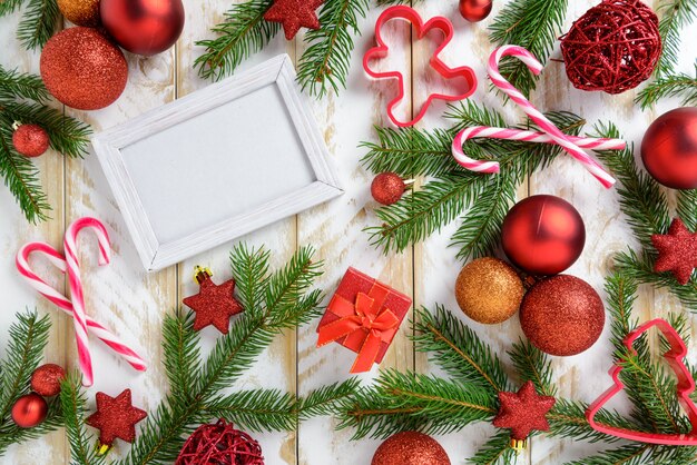 Cadre photo entre la décoration de Noël, avec des boules rouges et une canne en bonbon sur une table en bois blanche. Vue de dessus, cadre pour copier l'espace.