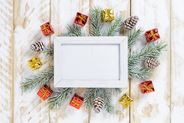 Cadre photo entre la décoration de Noël, avec des pommes de pin et des coffrets cadeaux sur une table en bois blanche. Vue de dessus, cadre pour copier l'espace