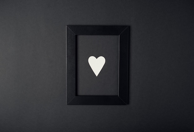 Cadre photo noir avec coeur Saint-Valentin blanc à l'intérieur sur le fond sombre (noir). Concept de la Saint-Valentin. Mise à plat, vue de dessus.