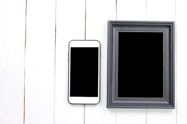 Cadre photo et smartphone sur un plancher en bois blanc.