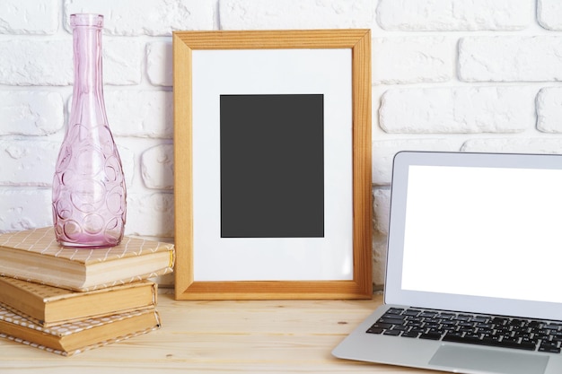 Cadre photo vide sur une table en bois avec des livres et un ordinateur portable