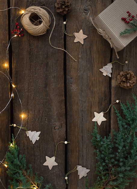 Cadre de planche de Noël et du nouvel an avec des branches de sapin, une guirlande brûlante, une boîte cadeau, des jouets en bois. Fond de bois rustique, espace copie.