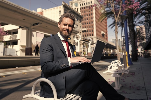 Un cadre professionnel joyeux tient un ordinateur en plein air avec un ordinateur portable sans fil moderne