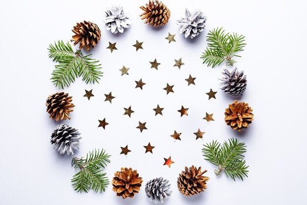 Cadre rond de Noël avec branches de sapin, pommes de pin peintes, confettis sur fond gris, espace de copie. Cadre rond avec décorations dorées et branches vertes