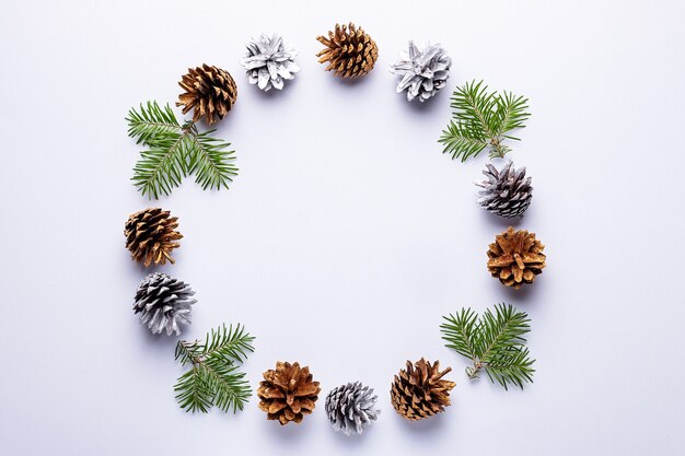 Cadre rond de Noël avec ornements dorés, branches de sapin, pommes de pin peintes, confettis sur fond gris, espace de copie. Couronne de Noël minimaliste