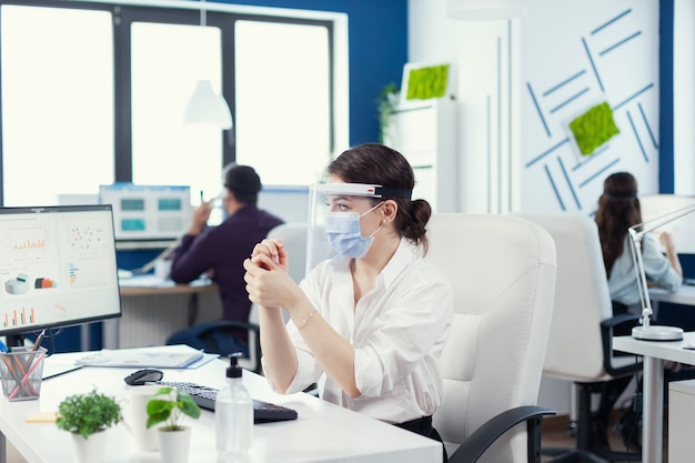 Un cadre se frottant les mains après avoir appliqué un désinfectant portant un masque facial pendant la pandémie mondiale avec covid19. Femme d'affaires dans un nouveau lieu de travail normal désinfectant pendant que ses collègues travaillent en b