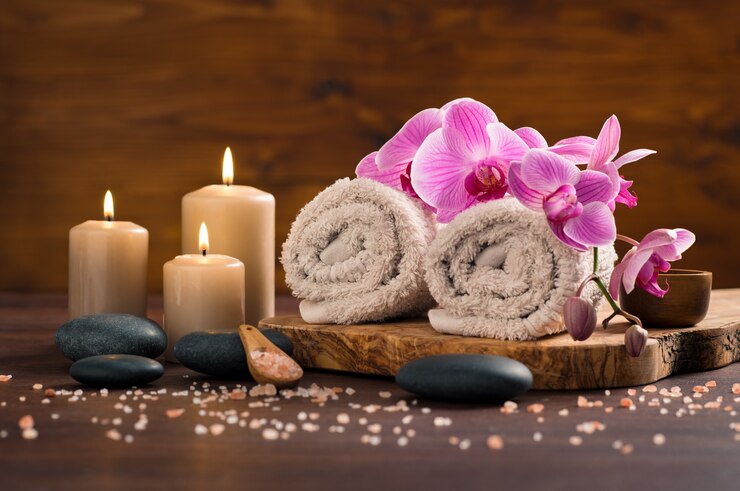 Cadre de spa avec serviette roulée brune et orchidées et bougies sur bois.