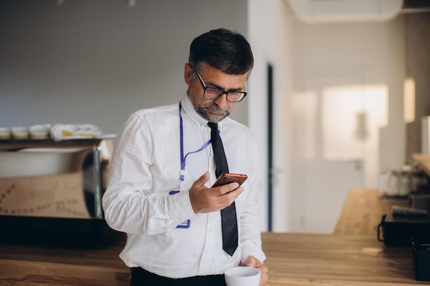 Cadre supérieur fatigué seul au bureau buvant du café et vérifiant les nouvelles sur phonexA