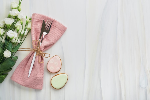 Cadre de table de brunch de Pâques Concept de vacances de Pâques de printemps avec assiette rose blanche et serviette avec symboles décoratifs œufs de lapin de vacances et bouquet de fleurs sur fond blanc Vue de dessus Maquette