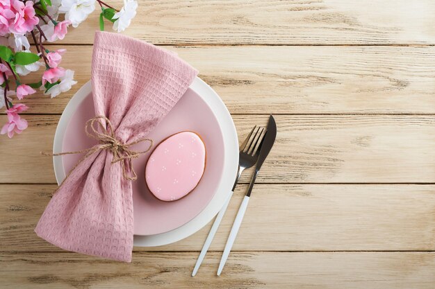 Cadre de table de brunch de Pâques Concept de vacances de Pâques de printemps avec assiette rose blanche et serviette avec symboles décoratifs oeufs de lapin de vacances et bouquet de fleurs sur fond en bois ancien Vue de dessus