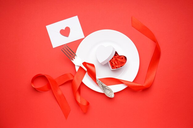 Cadre de table élégant et cadeau pour la Saint-Valentin sur fond rouge, vue de dessus.