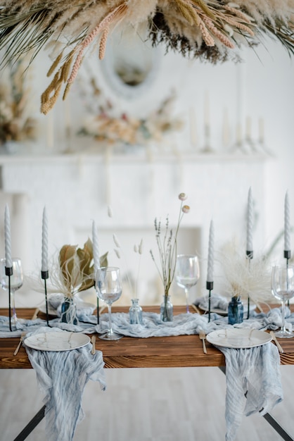 Cadre de table élégant avec des fleurs séchées. Assiette avec fourchette et couteau doré vintage, bougies, serviettes bleu poussiéreux sur table en bois. Décoration de mariage d'hiver.