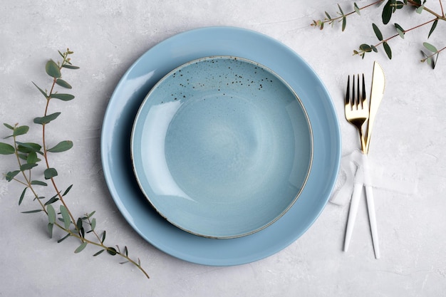 Cadre de table de fête avec assiette en céramique bleue ensemble de couverts dorés et feuilles d'eucalyptus fraîches sur une maquette d'assiette de table grise