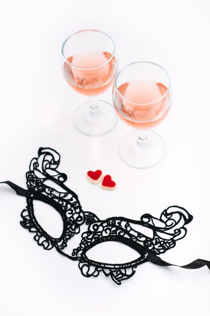 Cadre de table de fête saint valentin avec masque de dentelle noire deux verres de vin rosé et deux coeurs rouges