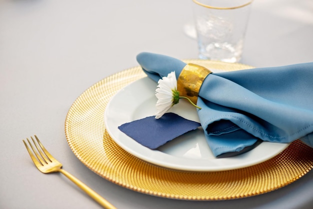 Cadre de table de mariage élégant et chic dans des couleurs or et bleu et des fleurs fraîches. Mise au point sélective douce.